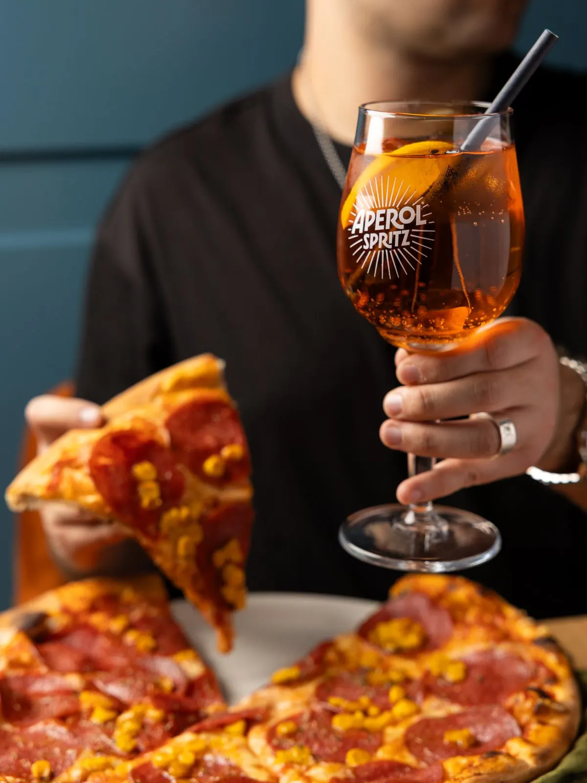 Aperol Spritz und ein Stück Pizza mit Salami und Mais