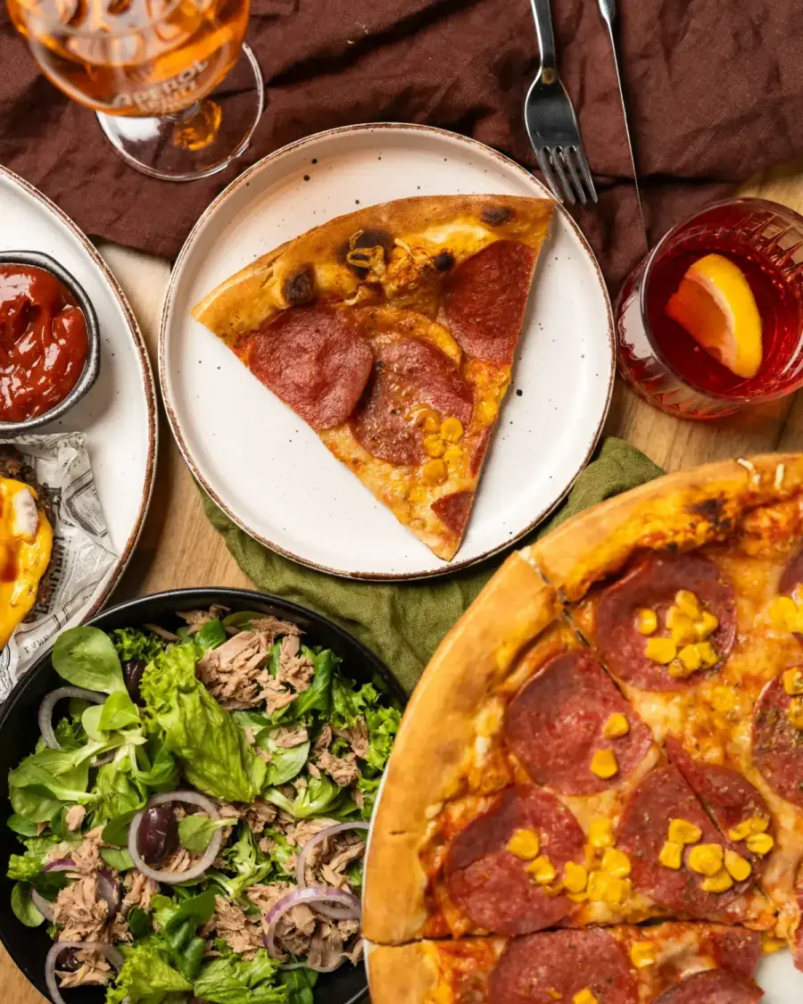 Pizza mit Puten-Salami und Mais, Thunfischsalat und Drinks auf dem Tisch