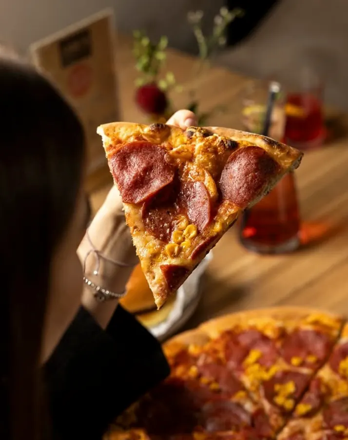 Pizza mit Salami und Mais, ein Stück wird abgehoben